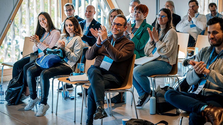 A group of attendees, wearing event lanyards, are seated in a bright conference room with large windows, clapping and smiling at the speaker during the Snowflake "Data for Breakfast" event.