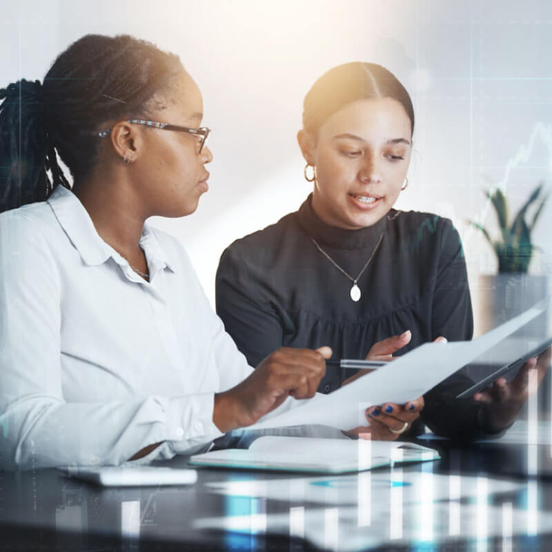  two woman working together at desk with data visual overlay